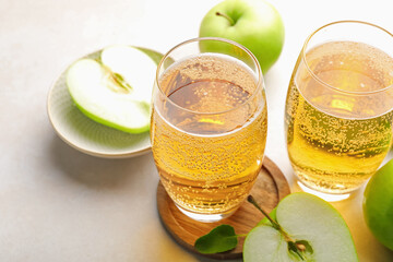 Fresh cider in glasses and apples on beige table, closeup