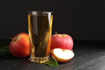 Fresh cider in glass, apples and green leaves on black table, space for text