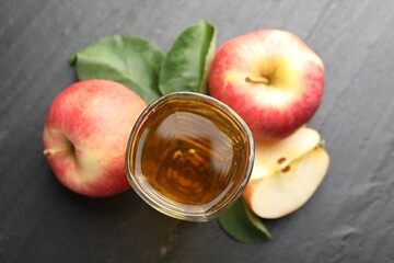 Fresh cider in glass, apples and green leaves on black table, flat lay