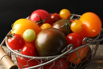 Different ripe tomatoes in basket on wooden table, closeup