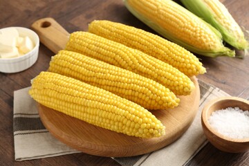 Tasty boiled corncobs, salt and butter on wooden table, closeup