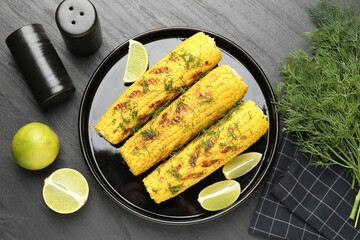 Tasty grilled corncobs with dill and lime slices on black table, flat lay