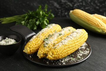 Tasty grilled corncobs with parsley and cheese on black table