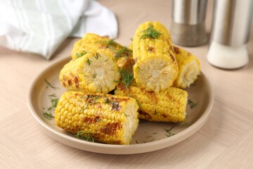 Pieces of tasty grilled corncobs with dill on wooden table, closeup