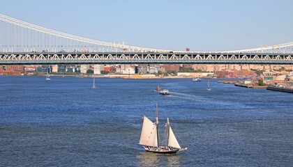 Fototapeta premium Sunny day on the East River in New York City and Manhattan Bridge and an schooler sails on blue waters