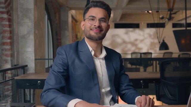 Pensive Indian business man working with papers businessman smiling in camera nodding head yes satisfied in office Arabian ethnic guy male specialist writing documents information with laptop happy