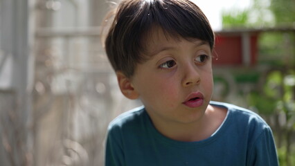 Young boy looking intently to the side, with a thoughtful expression on a sunny day. the quiet moment of a child lost in thought, surrounded by the greenery of the outdoors-SD 480p