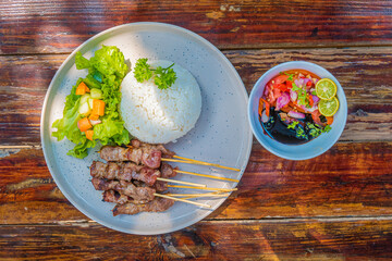 Delicious grilled meat skewers with rice, salad, and sauce on rustic wooden table