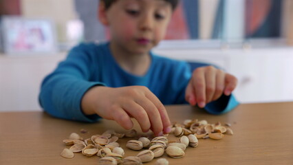 Young boy eating pistachio nuts at a table, carefully selecting and enjoying his snack. a simple moment of a child savoring a healthy treat, focused on the act of eating-SD 480p