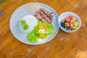 Delicious grilled skewers with rice, fresh salad, and vibrant side dish on wooden table