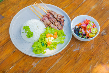 Delicious grilled satay, rice, and fresh salad served on a wooden table for a tasty meal