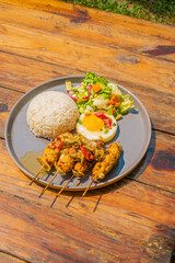 Delicious gourmet meal with rice, skewers, egg, and fresh salad on a rustic wooden table setting