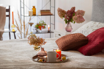 cup of coffee on tray with candle on bed
