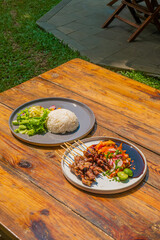 Delicious Indonesian satay with rice and fresh salad served on a rustic wooden table in sunlight