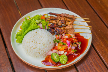 Delicious Indonesian satay with rice, salad, and lime wedges on a wooden table setting