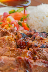 Delicious grilled meat with rice and fresh salad, drizzled with savory sauce for a meal