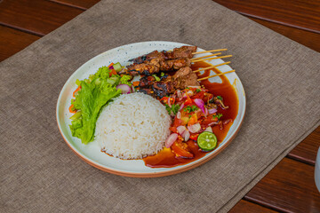 Delicious Indonesian Sate served with rice, fresh vegetables, and a vibrant chili sauce