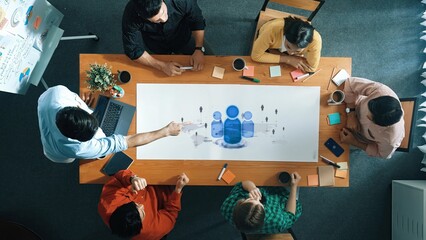 A diverse team participates in a collaborative meeting around a conference table, focusing on strategy and creative ideas for business growth in a modern office environment. Raster