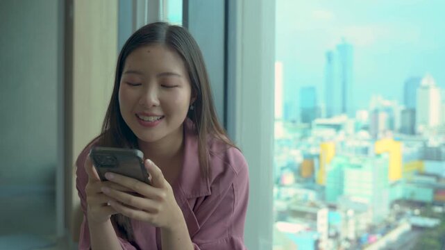 Happy young woman sitting on sofa holding phone smiling enjoying using mobile apps for shopping, having fun playing games, chatting on social media at office