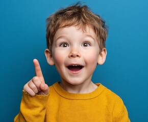 A young boy with a bright, expressive face, pointing upward, displays a joyful and enthusiastic expression against a bold blue backdrop.
