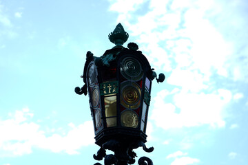 Ornate wrought iron lantern with stained glass panels stands against blue sky, symbolizing artistic craftsmanship, vintage elegance, and urban charm