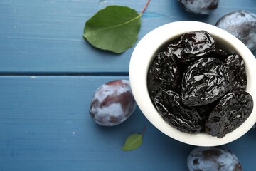 Dried prunes and fresh plums on blue wooden table, flat lay. Space for text