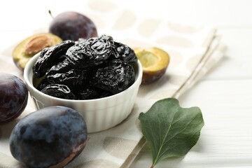 Dried prunes, fresh plums and green leaf on white wooden table, closeup