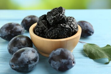 Dried prunes in bowl, leaf and fresh plums on light blue wooden table, closeup