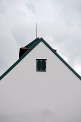 Minimal white house facade with triangular roof and small shuttered window stands against cloudy sky, symbolizing simplicity, geometry, and architectural clarity.