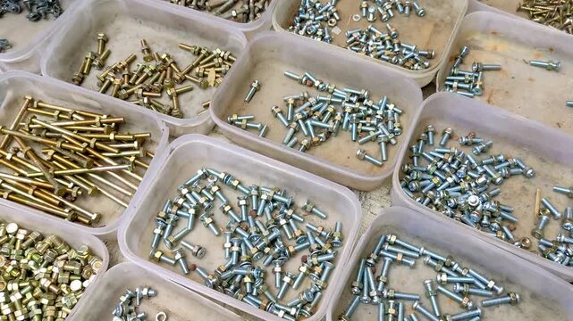 Several small clear plastic containers filled with various types of metal fasteners, namely bolts and screws. The items are sorted by shape and type.