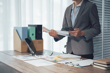 Organized Workspace: A business person, dressed in professional attire, carefully sorts through essential documents and files in their tidy office setting.