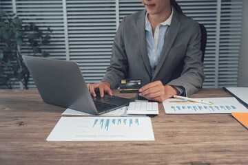 Focused Professional at Work: An accomplished professional, fully engrossed in her work, meticulously reviews data and engages with a laptop on her desk, surrounded by financial documents.