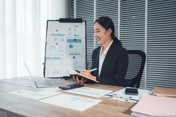 Focused Woman at Work: An intelligent business woman is deep in concentration, taking notes and utilizing technology with charts in the background.