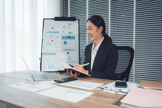 Focused Woman at Work: An intelligent business woman is deep in concentration, taking notes and utilizing technology with charts in the background.