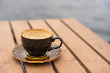 Rustic ceramic cup and saucer on wooden table at waterfront cafe in Bergen, Norway. The coffee is finished, leaving only traces in the cup. Scene captures quiet moment by the sea