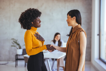 Diverse Women Shaking Hands and Smiling in a Modern Office Setting