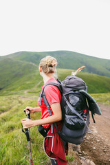 young woman's view back with a large backpack looking at mountain ranges and peaks, in the mountains, hiking, travel, atmospheric photo