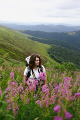 woman tourist with a large backpack on the background of a mountain landscape hiking through wildflowers pink Ivan tea flowers, female traveller,  travel, Carpathian