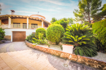Villa in the garden with a driveway and garage on a sunny day.