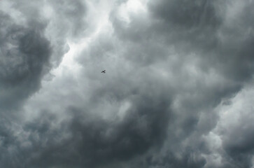 Small sport airplane flying into storm with dramatic cumulus clouds and gray sky creating powerful aviation and weather background concept