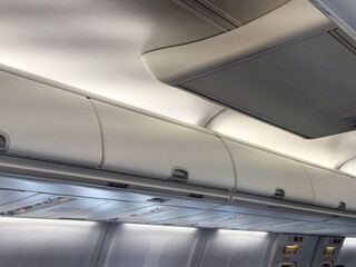 Fototapeta premium Overhead luggage compartments and cabin ceiling inside a passenger airplane. Travel, aviation, and the practical design of space in modern aircraft cabins.