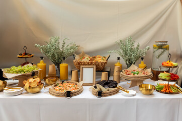 Catering buffet displaying gourmet appetizers, desserts, and drinks arranged on green-adorned table with fresh eucalyptus branches