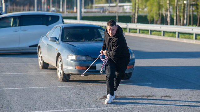 Caucasian man pulling a car with a rope. 