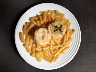 raw pasta on a white plate with rosemary on a black background