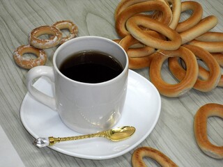 A white mug with tea on a white saucer. Around the mug are placed bagels and pretzels, some of which are covered with powdered sugar.