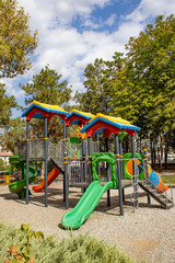 Bright plastic playset with tunnel slide, spiral slide and seesaw in a green park. Useful for education, recreation, childcare brochure, urban planning article, parenting blog or safety guide.