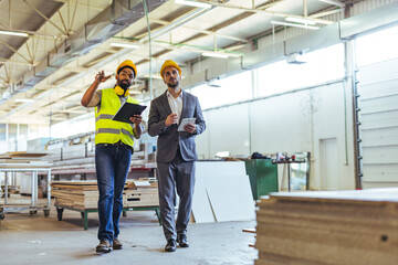 Two Engineers Discussing in a Factory Warehouse Wearing Hard Hats and Safety Gear