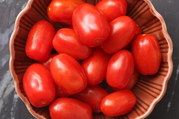 Fresh cherry tomatoes in bowl. Red vegetable closeup on dark background. Healthy food ingredient for salad. Organic ripe tomato fruits. Vegetarian cooking ingredient. Natural plant based diet.