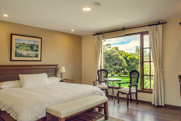 habitación con cama amplia, decoración elegante y ventanales que ofrecen una vista luminosa al jardín verde. Un espacio sereno y confortable ideal para el descanso y la conexión con la naturaleza