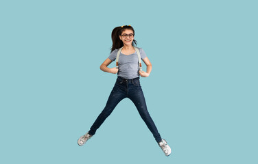 Excited Indian teen schoolgirl with backpack jumping up in air on blue studio background. Emotional teenager smiling and flying, happy to start school, enjoying college education